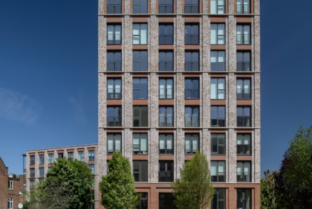Modern multi-story office building with brick facade, large windows, and surrounding greenery.